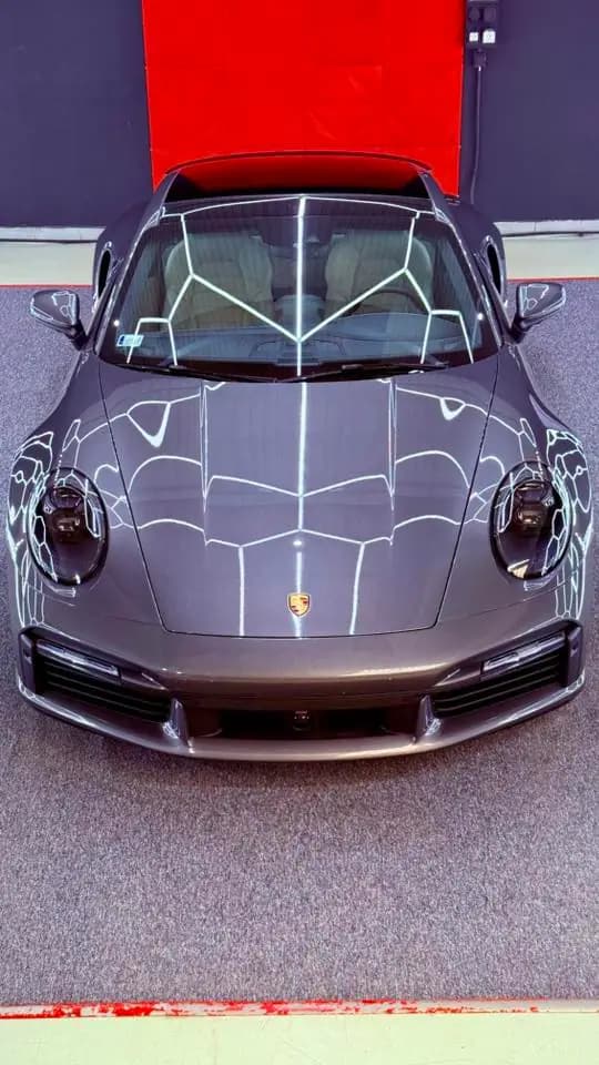 Szürke Porsche 911 szemből, tükörfényes felülettel a műhelyben